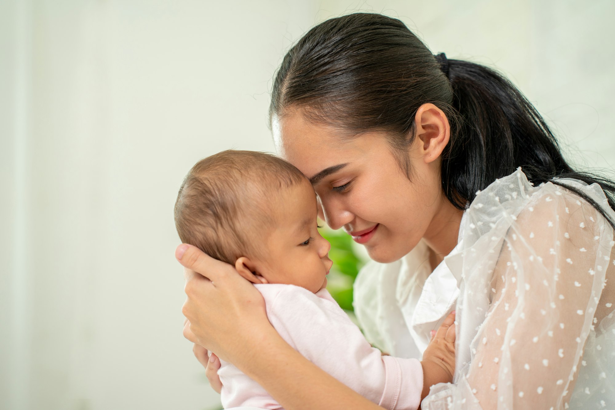 Loving Asian Mom carying of her newborn baby at home in the bedroom. happy family.